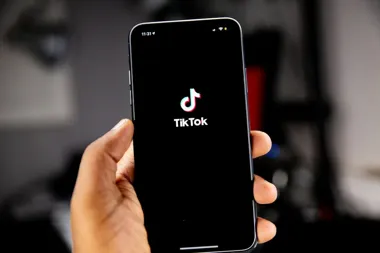 Dłoń trzyma smartfon z logo TikToka na czarnym ekranie.