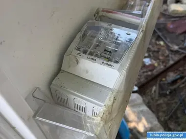 Zbliżenie na uszkodzony lub porzucony rozdzielacz elektryczny z oznaczeniami 160A i 690V, umieszczony w drewnianej skrzyni na zewnątrz budynku.